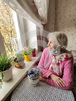 The Covid-19, health, safety and pandemic concept - senior old lonely woman sitting near the window