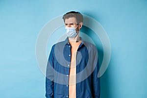 Covid-19 and healthcare concept. Dissatisfied frowning guy in medical mask looking at bad promo, stare aside at empty