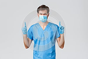 Covid-19, healthcare workers and hospital concept. Serious-looking male doctor in blue scrubs, medical mask and gloves