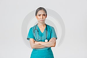 Covid-19, healthcare workers, pandemic concept. Skeptical and reluctant asian female doctor, tired nurse in scrubs cross