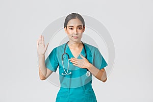 Covid-19, healthcare workers and preventing virus concept. Smiling honest asian female doctor, intern in scrubs giving