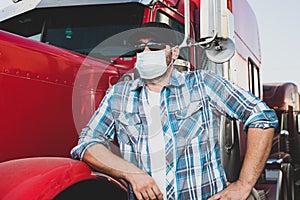 Covid-19 impacting the transportation  industry concept with truck driver wearing safety face mask next to big rig. Confident truc