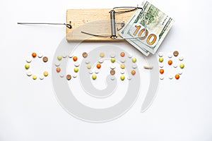 Covid-19 inscription with pills and capsules and hundred dollar bill caught in a wooden mousetrap in layout on a white