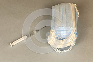 COVID-19. A lot of disposable protective masks and a syringe on a gray background. Selective focus