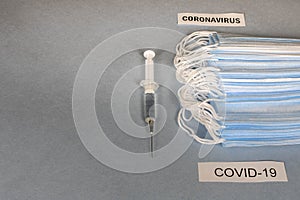 COVID-19. A lot of disposable protective masks and a syringe on a gray background. Selective focus