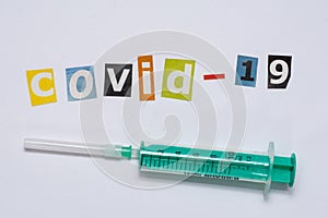 The COVID 19 message written in cut-out letters next to a neddle syringe