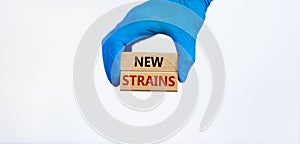 Covid-19 new strains symbol. Hand in blue glove holds wooden blocks, words `new strains`. Beautiful white background. Copy space