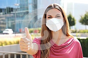 COVID-19 Optimistic business woman wearing protective mask KN95 FFP2  showing thumbs up in modern city street