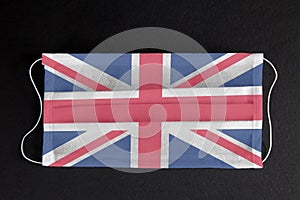Covid-19 outbreak in Great Britain. Coronavirus update in UK. Union Flag printed on medical mask on black background.