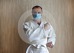 COVID-19 Pandemic Coronavirus concept. A young strong man in a white kimono for sambo, jiu jitsu and other martial arts with a
