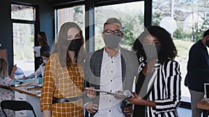 COVID-19 safety at workplace. Happy young multiethnic colleagues look at camera wearing face masks at modern office.