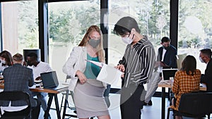 COVID-19 safety at workplace. Happy young multiethnic colleagues working with documents wearing masks at modern office.