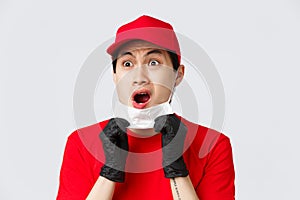 Covid-19, self-quarantine online shopping and delivery concept. Shocked and freak out asian courier in protective gloves