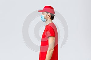 Covid-19, self-quarantine, online shopping and shipping concept. Profile of serious young courier in red uniform of