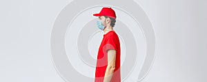 Covid-19, self-quarantine, online shopping and shipping concept. Profile of serious young courier in red uniform of