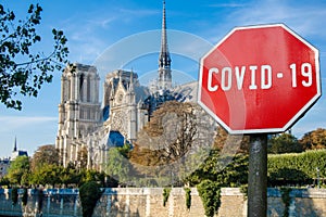 COVID-19 sign against view of Notre Dame de Paris or Notre-Dame Cathedral in Paris
