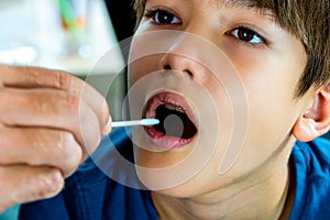 Covid-19 test in elementary age child. A hand holding a cotton oral swab sample from childâ€™s mouth to analyze the saliva, mucous