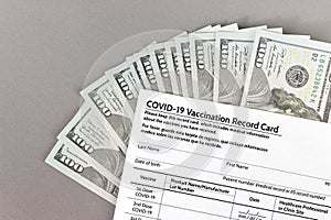 COVID-19 Vaccination Record Card, coronavirus immunization certificate with several 100 US money notes spread out in fan shape.