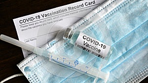 COVID-19 vaccine bottle, syringe, surgical mask and coronavirus Vaccination Record Card