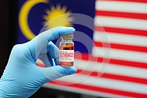 COVID-19 vaccine. Malaysian doctor or frontliner wearing blue gloves holding vaccine in a clear glass bottle with Malaysia flag