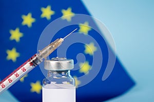 COVID-19 vaccine vial against EU flag on blue background with copy space for text - coronavirus vaccine doses, europe vaccination