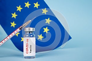 COVID-19 vaccine vial against EU flag on blue background with copy space for text - coronavirus vaccine doses, europe vaccination