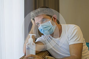 Covid-19 virus lockdown - sad and worried man covered with medical mask washing hands with sanitizer gel in home quarantine