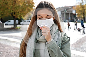 COVID-19 Young woman coughs with surgical mask during coronavirus pandemic disease in city street. Girl having symptoms like