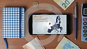 Covid-19 economic crisis: a smartphone with a question about mes or eurobond on a wooden desk with some office objects photo