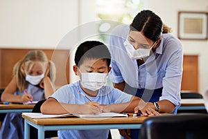 Covid, education and learning with a teacher wearing a mask and helping a male student in class during school. Young boy
