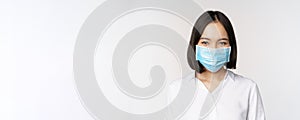 Covid and healthcare concept. Close up portrait of asian woman, office lady in face mask, smiling, using protection from