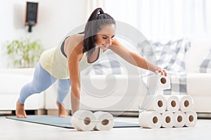 Covid-inspired workout by a fit woman stacking toilet paper rolls in a plank position