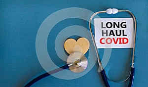 COVID-19 long-haul covid symptoms symbol. White card with words Long haul covid. Wooden heart, stethoscope, beautiful blue photo