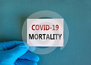 Covid-19 mortality symbol. Hand in blue glove with white card. Concept words `Covid-19 mortality`. Medical and COVID-19 pandemic photo