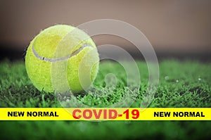 Covid-19 and new normal words on yellow line with tennis ball on green grass background