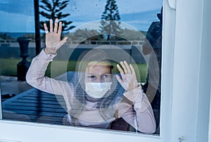 COVID-19 Quarantine. Sad little girl looking through the window feeling lonely during lockdown photo