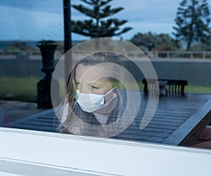 COVID-19 Quarantine. Sad little girl looking through the window feeling lonely during lockdown photo
