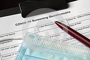 COVID-19 Screening Questionnaire form with medical mask and a pen on it. Healthcare and medical concept. Closeup photo