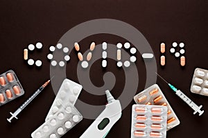 Covid-19 text written with medical pills with syringes, thermometer on brown background