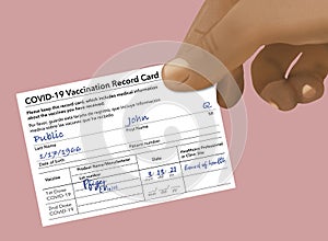 A Covid-19 Vaccination Record Card that is generic and filled out with John Q PublicÃ¢â¬â¢s name is held by a hand photo