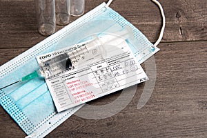 Covid-19 vaccination record cards and Syringe with vaccine and mask on the table photo