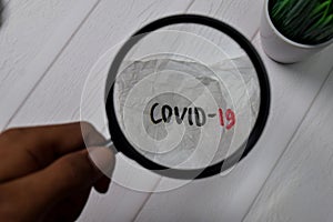 Covid-19 write on crunched paper with magnifying glass isolated on wooden table photo