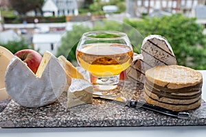 Cow cheeses of Normandy - camembert, livarot, neufchatel, pont l`eveque and glass of apple cider drink with houses of Etretat