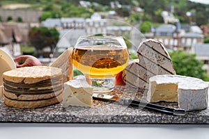 Cow cheeses of Normandy - camembert, livarot, neufchatel, pont l`eveque and glass of apple cider drink with houses of Etretat