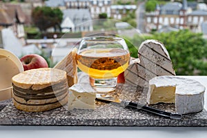 Cow cheeses of Normandy - camembert, livarot, neufchatel, pont l`eveque and glass of apple cider drink with houses of Etretat