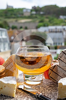 Cow cheeses of Normandy - camembert, livarot, neufchatel, pont l`eveque and glass of apple cider drink with houses of Etretat