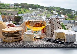 Cow cheeses of Normandy - camembert, livarot, neufchatel, pont l`eveque and glass of apple cider drink with houses of Etretat