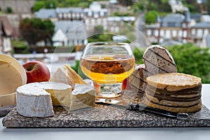 Cow cheeses of Normandy - camembert, livarot, neufchatel, pont l`eveque and glass of apple cider drink with houses of Etretat