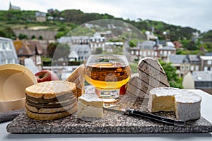 Cow cheeses of Normandy - camembert, livarot, neufchatel, pont l`eveque and glass of apple cider drink with houses of Etretat