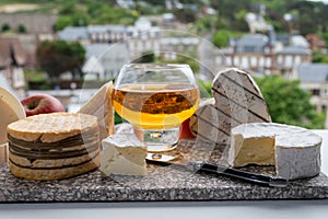 Cow cheeses of Normandy - camembert, livarot, neufchatel, pont l`eveque and glass of apple cider drink with houses of Etretat